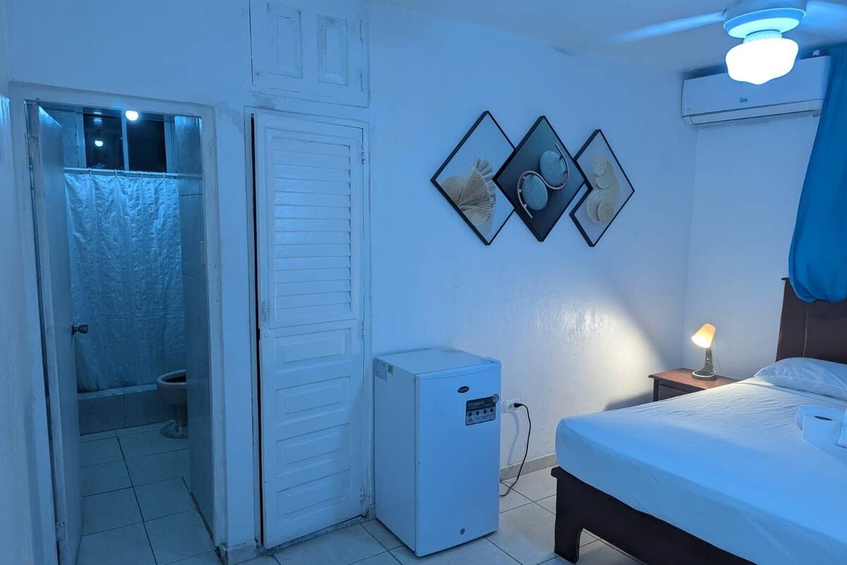 Un dormitorio con cama, una mesita de noche con lámpara, un pequeño calefactor y un aire acondicionado instalado en la pared.