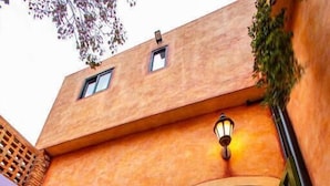 Un bâtiment doté d’une façade orange à texture, d’une porte verte et d’un hall d’entrée carrelé agrémenté de plantes en pot.