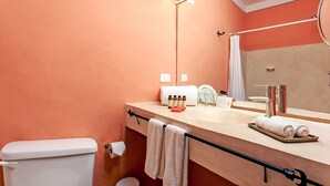 Kylpyhuone, jossa on beigenvärinen pesuallas, peili, pyyhekoukku ja hygieniatarvikkeita.