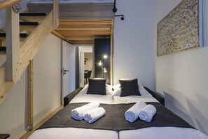A hotel room with a wooden staircase, a bed with white linens, two black pillows, and a large abstract painting on the wall.