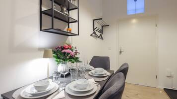 A dining area with a table set for four, a vase of flowers, and a black metal shelf above.