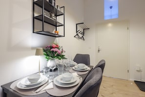 Un coin repas avec une table dressée pour quatre personnes, un vase de fleurs et une étagère en métal noir au-dessus.