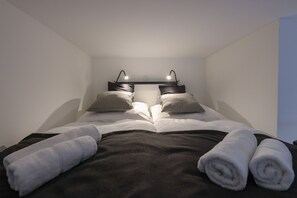 Ein ordentlich bezogenes Bett mit zwei Kissen, einem Kopfteil mit zwei Leselampen und zwei zusammengerollten Handtüchern auf dem Bett.