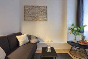 Ein modernes Wohnzimmer mit einem dunklen Sofa, einem Glaskerzenhalter, einem runden Tisch mit Obstschale und einem Wanddekor.