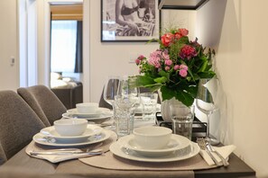 Une table à manger dressée avec de l’assiette blanche, des bols, des verres et des couverts, agrémentée d’un arrangement floral au centre.