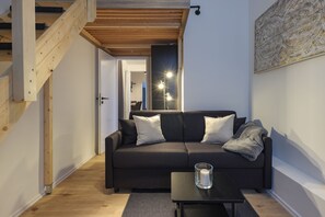 A modern living room with a dark sofa, a glass candle holder, and a wooden staircase.