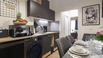 A modern kitchen with a dishwasher, microwave, and coffee maker. There is a dining area with a table set for two, and a framed picture on the wall.