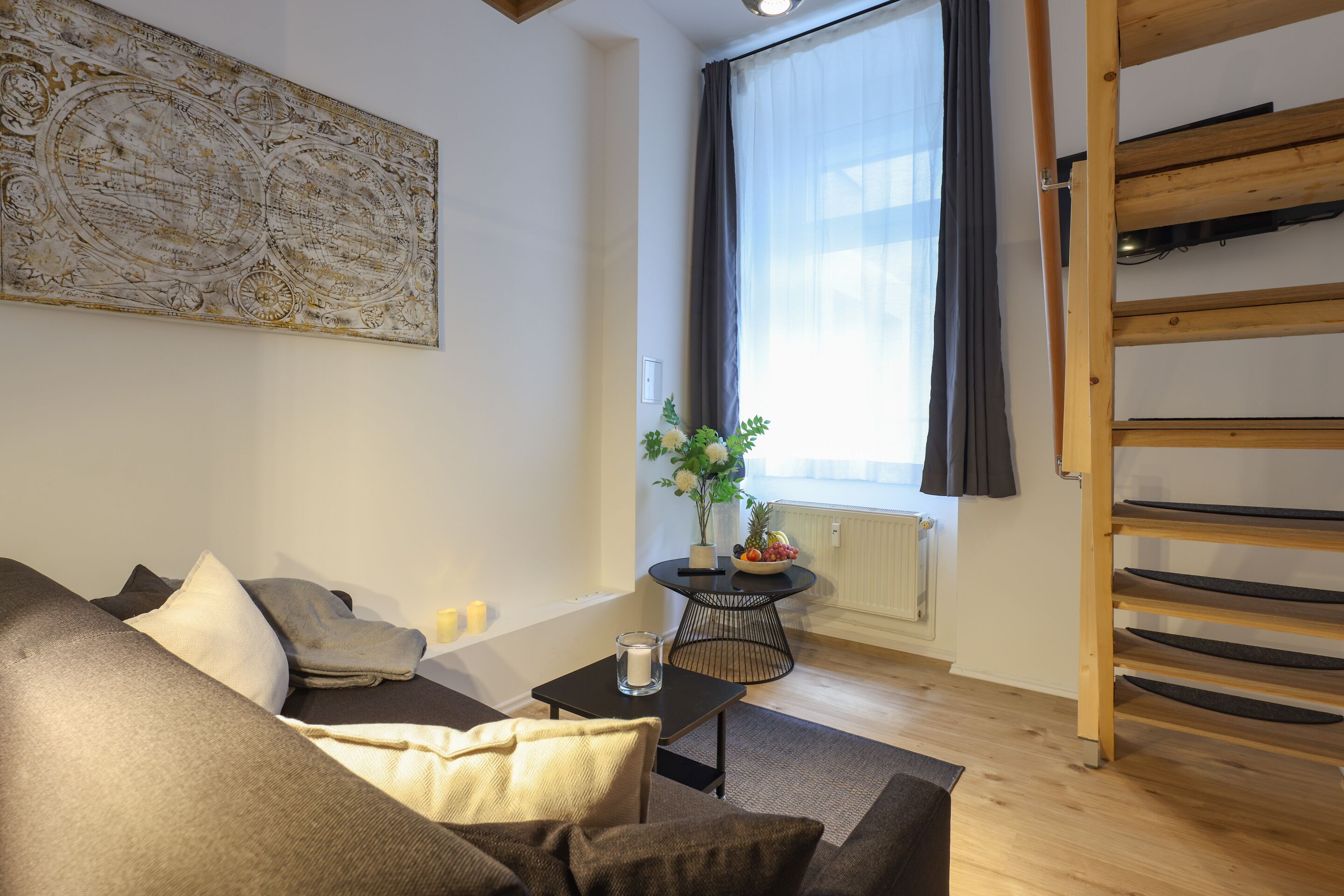 A modern living room with a sofa, a small table with a candle, a decorative wall piece, a window with curtains, and a wooden shelf.