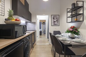 Eine moderne Küche mit Holzarbeitsplatte, einem integrierten Geschirrspüler und einer Mikrowelle. Es gibt einen Essbereich mit einem Tisch für zwei Personen, einer Blumenvase und einer schwarzen Regaleinheit darüber.