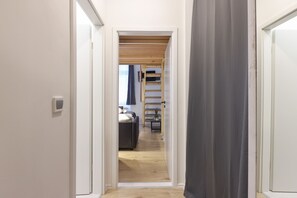 Ein schmales Gangbett zu einem Schlafzimmer mit einem Bett, einer Holzleiter und einem kleinen Tisch mit einer Pflanze.