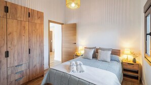 Et soveværelse med en stor garderobe, en seng med hvid dyne, to sengeborde med lamper og et vindue med udsigt.