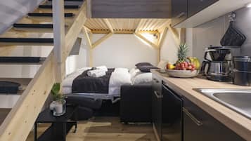 Un dormitorio compacto con zona de descanso elevada, una kitchenette pequeña y una escalera de madera.
