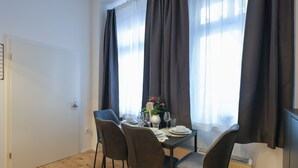 Un comedor con una mesa dispuesta para cuatro, sillas, un jarrón con flores y un radiador.