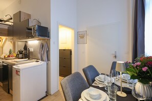 A modern kitchen with a microwave, sink, and a small refrigerator. There is a dining area with a table set for two, including plates, glasses, and a vase with flowers.