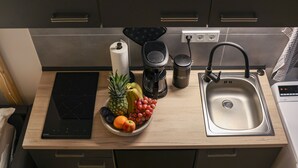 Uma cozinha com um fogão por indução moderno, uma cafeteira, uma pia e uma cesta de frutas.
