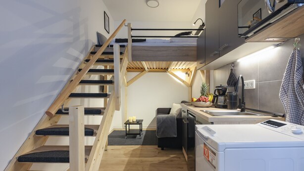 Una cocina compacta con lavadora integrada, una escalera de madera y una pequeña zona de estar.
