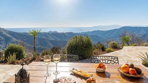 A table with wine glasses, a basket of fruit, and a plate of fries, set against a scenic mountain backdrop. - Atalaya Málaga by Ruralidays (Málaga)