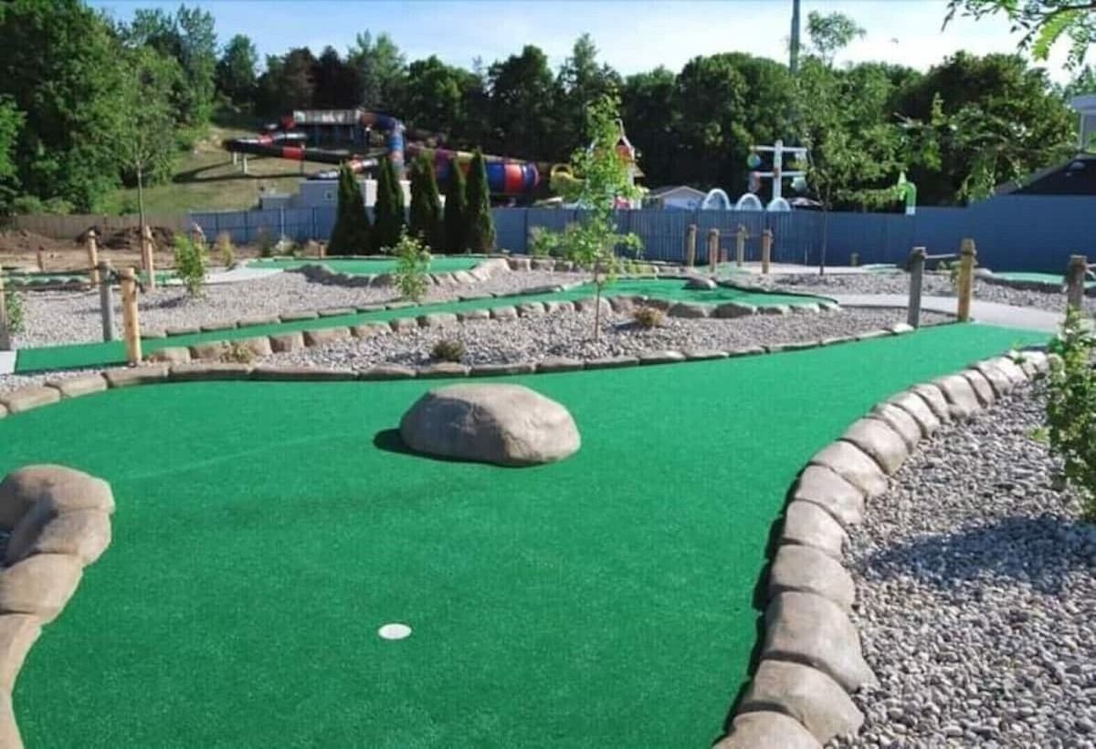 Un campo de mini golf con superficie verde, una pelota blanca y algunos obstáculos.