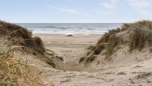 Uma praia com dunas de areia e o oceano ao fundo.