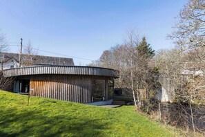 A circular building with a covered porch, a grassy area in front, and a river nearby. - Otters Holt Circular Riverside Retreat with Hot Tub (Killin)