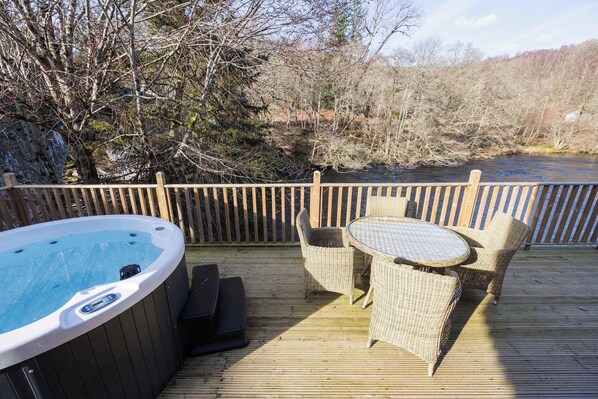 A wooden deck with a hot tub, wicker chairs, and a table. - Otters Holt Circular Riverside Retreat with Hot Tub (Killin)