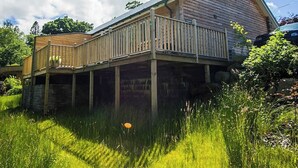 Ett trähus med en veranda, omgivet av frodig grönska.