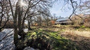 Ett hus med en veranda, omgivet av träd och en liten bäck.