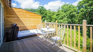A wooden deck with a hot tub, a table, and chairs. - Cosy Riverside Escape with Hot Tub | Garth Cottage (Killin)