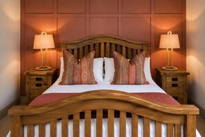 Een houten bed met een gebogen hoofdeinde, twee nachtkastjes met lampen en gestreepte kussens.