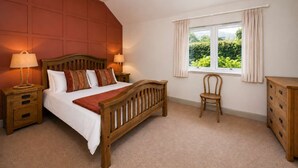 A bedroom with a wooden bed, two bedside tables, a nightstand, a chair, a dresser, and a window with curtains. - Cosy Riverside Escape with Hot Tub | Garth Cottage (Killin)