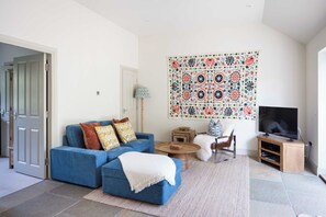 Ein Wohnzimmer mit einem blauen Sofa, einem Fernseher, einem Wandbehang mit Muster und einem kleinen Tisch.
