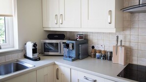 A kitchen with white cabinets, a coffee machine, a microwave, a toaster, and a knife block. - Cosy Riverside Escape with Hot Tub | Garth Cottage (Killin)