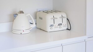 A kitchen with a white cabinet above a countertop. On the countertop, there is a white electric kettle and a white toaster with control knobs and a power cord. - The Tractor Shed- Elevated Hot Tub with Loch Views (Acharn)