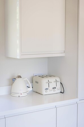 A kitchen with a white cabinet above a countertop. On the countertop, there is a white electric kettle and a white toaster with control knobs and a power cord.