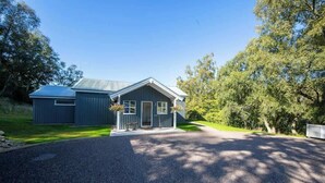 A modern two-story house with a metal roof, a driveway, and a well-maintained lawn. - The Tractor Shed- Elevated Hot Tub with Loch Views (Acharn)
