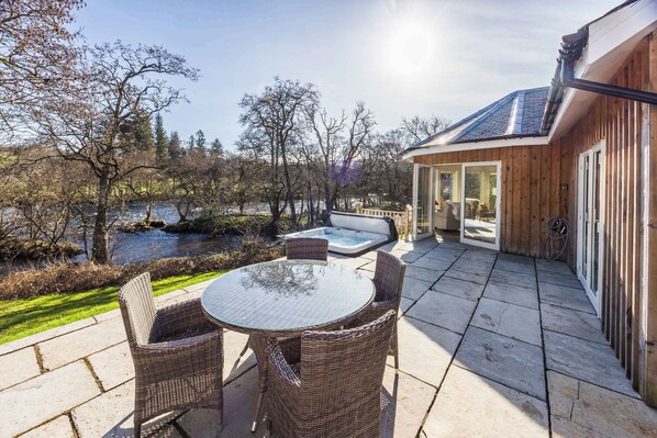 Un patio con mobiliario de mimbre, un jacuzzi y una construcción de madera con techo inclinado.