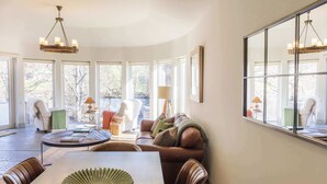 A spacious living area with a dining table, leather chairs, a brown leather sofa, and a large window offering a view of the outdoors. - Luxury Riverside Lodge with Hot Tub (Sleeps 6) (Killin)