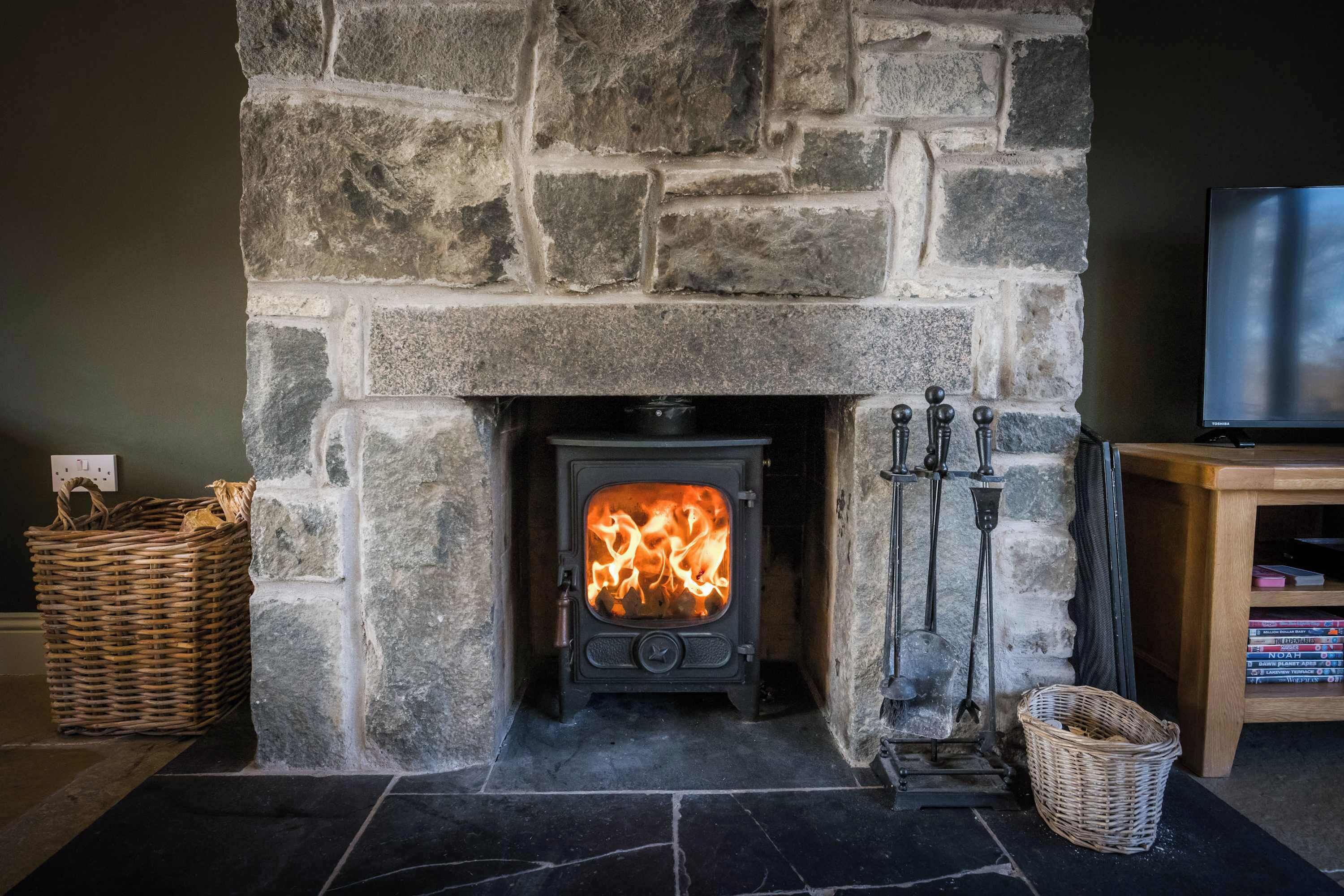 Una chimenea de piedra con estufa de leña, un televisor sobre un soporte de madera y una cesta en el suelo.