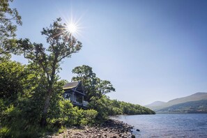 A lakeside cabin with a view of the water and hills in the background. - Osprey Boathouse Over Loch Tay with Hot Tub (Acharn)