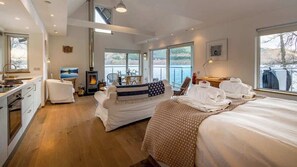 A modern hotel room with a large bed, a sofa, a fireplace, and a view of the lake. - Osprey Boathouse Over Loch Tay with Hot Tub (Acharn)