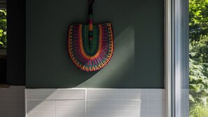 Un baño con una bañera blanca, un ventanal con vistas a la vegetación y un adorno tejido y colorido en la pared.