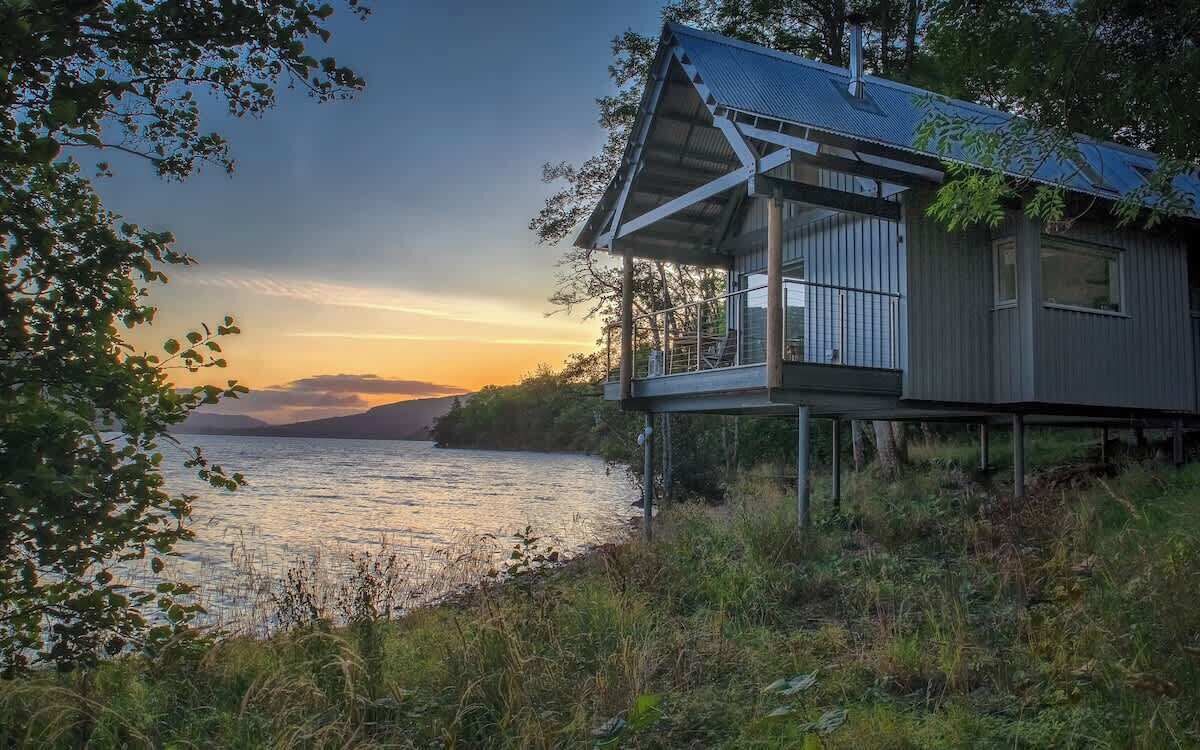 Een modern huis met balkon, met uitzicht op een waterpartij, omringd door bomen.