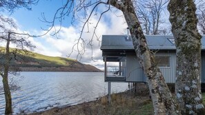A lakeside cabin with a balcony overlooking the water, surrounded by trees and hills. - Osprey Boathouse Over Loch Tay with Hot Tub (Acharn)