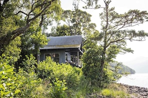 A house surrounded by dense foliage, with a view of the water in the background. - Osprey Boathouse Over Loch Tay with Hot Tub (Acharn)
