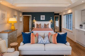 Un dormitorio con cama, mesitas de noche, lámpara, sofá y ventana.