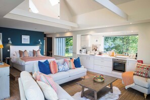 Un espacio habitable moderno con cama, sofá y zona de comedor, que cuenta con un ventanal con vistas a zonas verdes.