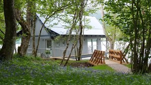 A cabin with a sloped roof, surrounded by trees and a garden with blue flowers. - Dipper Boathouse Secluded Over-Water Retreat (Acharn)