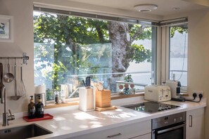 Una cocina moderna con un ventanal amplio, electrodomésticos de acero inoxidable y vistas a árboles.