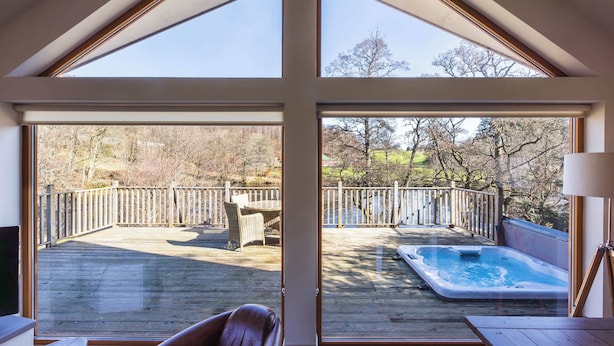 A spacious deck with a hot tub, wooden deck, and a view of trees and a fence. - Riverbank- Glass-Fronted Riverside Stay -Hot Tub (Killin)