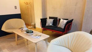 Ein modernes Wohnzimmer mit einem hellen Sofa, einem roten und schwarzen Sofa mit gemusterten Kissen sowie einem Couchtisch aus Holz mit dekorativen Gegenständen.